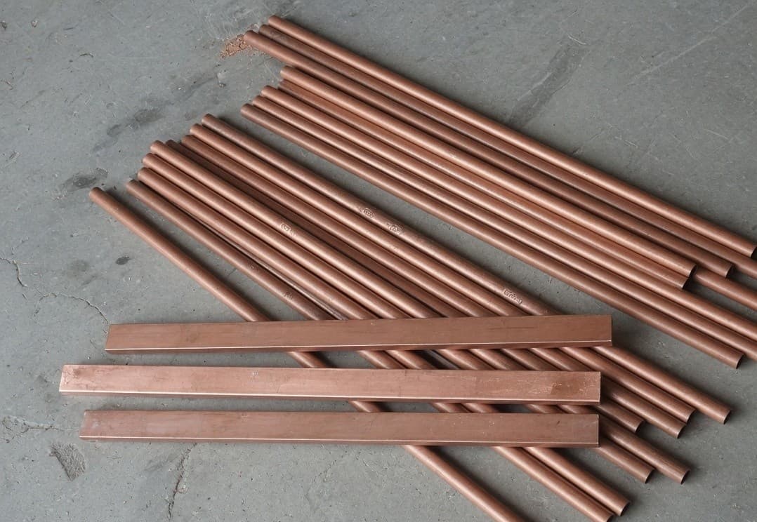 Clean dull copper pipes and flat copper busbar on a concrete floor